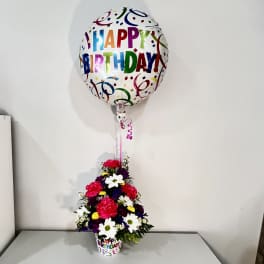 Birthday balloon above a colorful flower arrangement in a printed cup