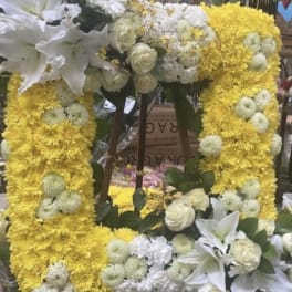 Yellow floral wreath with white lilies and roses on a stand