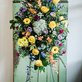 Tall mixed floral spray on a stand with yellow roses and purple blooms