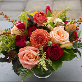 Mixed bouquet of roses, dahlias, and tulips in a glass vase
