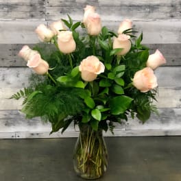 Pale pink roses arranged in a clear glass vase with lush greenery