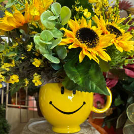 Yellow sunflower arrangement in a smiley-face mug vase