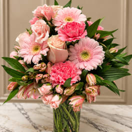 Pink gerberas, roses, and carnations in a clear glass vase