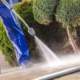 Person in blue protective pants pressure-washing a paved surface outdoors