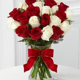 Arrangement of red and white roses in a clear vase with a red bow