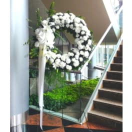 White floral wreath on a stand with a long white ribbon in an indoor lobby