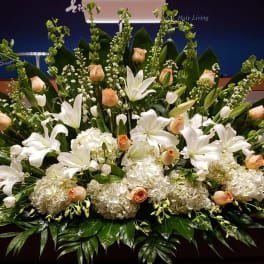 Low, wide arrangement of white lilies, hydrangeas, and peach roses on a stage