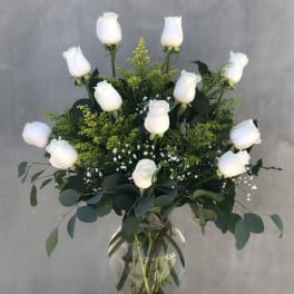 White roses arranged in a clear glass vase with green foliage.