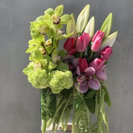 Arrangement of green orchids, pink tulips, and lilies in a glass vase