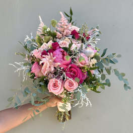 Handheld bouquet of pink roses and peonies with airy greenery