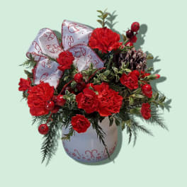 Red carnation arrangement in a white vase with a large ribbon bow