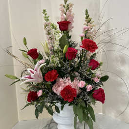 Tall bouquet of red roses, pink lilies, and carnations in a white vase