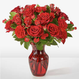 Red roses and carnations arranged in a red glass vase