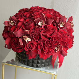 Red rose bouquet with burgundy orchids in a black vase