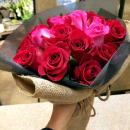 Hand-tied bouquet of red and pink roses wrapped in black paper and burlap