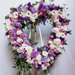 Heart-shaped floral wreath with pink, white, and purple blooms on a stand