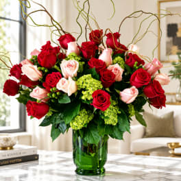 Red and blush roses arranged in a green glass vase with curly branches