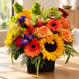 Colorful bouquet of sunflowers, roses, gerbera daisies, and orchids in a black vase