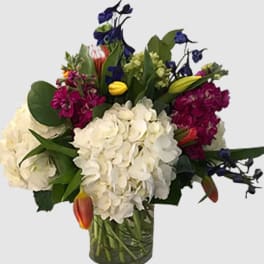 Mixed bouquet with white hydrangeas, purple blooms, and tulips in a glass vase