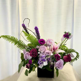 Purple and pink floral arrangement in a black square vase