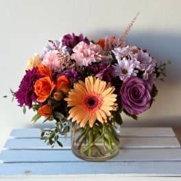 Mixed bouquet in a clear glass vase with purple, pink, orange, and peach flowers