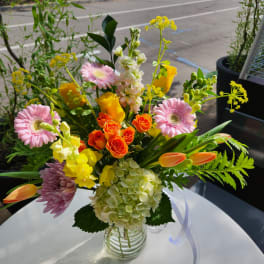 Mixed bouquet in a clear glass vase with pink gerberas, orange roses, and yellow blooms
