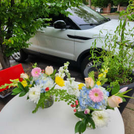 Two floral centerpieces in glass vases on a white table outdoors