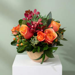 Orange roses and burgundy orchids arranged in a beige bowl