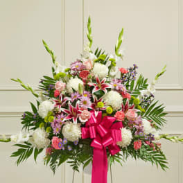 Large standing floral arrangement with pink, white, and purple flowers and a bright pink ribbon