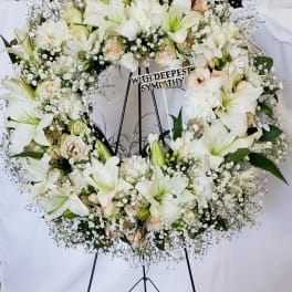 White sympathy wreath on a black stand with lilies and roses