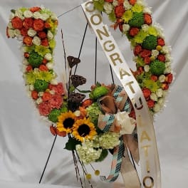 Floral wreath with orange and white roses, sunflowers, and a congratulatory ribbon