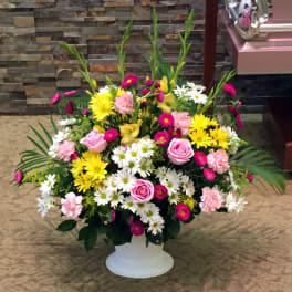 Mixed pink, yellow, and white flowers arranged in a white pedestal vase
