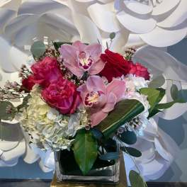 Square vase arrangement with pink orchids, red and hot pink roses, and white hydrangea.
