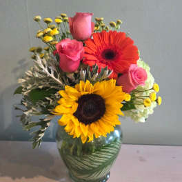 Bouquet of pink roses, sunflowers, and a red gerbera daisy in a glass vase