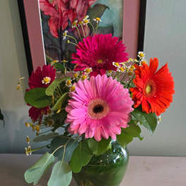 Bright pink and orange gerbera daisies with small white daisies in a clear glass vase.