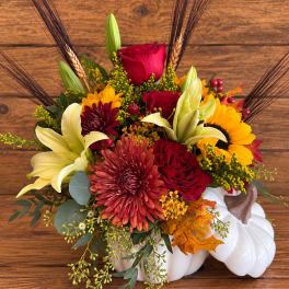 Autumn floral arrangement in a white pumpkin container with red, yellow, and cream blooms