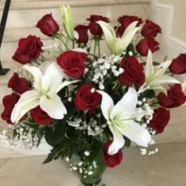 Tall arrangement of red roses and white lilies in a clear glass vase
