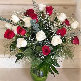 Tall arrangement of red and white roses with baby's breath in a clear glass vase