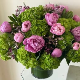 Low round arrangement of bright green hydrangeas and pink peonies in a clear glass cylinder vase.