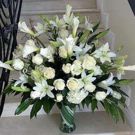 Tall white arrangement of roses, lilies, and calla lilies in a clear glass vase