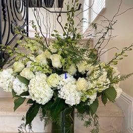 Large white hydrangeas and roses with green orchids in a tall glass cylinder vase