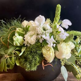 White floral arrangement in a black vase with green accents