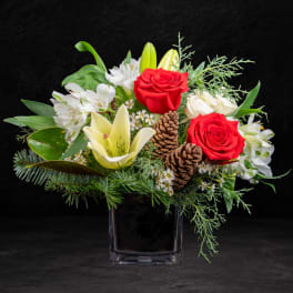 Red roses and white lilies in a black glass vase with pinecones