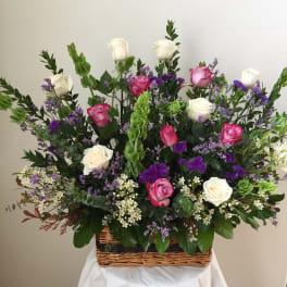 Basket arrangement of pink and white roses with purple filler flowers