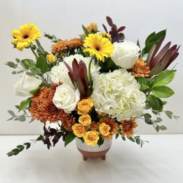 Mixed bouquet of white roses, hydrangeas, and yellow gerberas in a ceramic vase