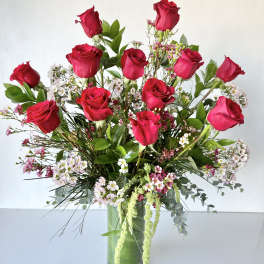 Tall bouquet of red roses and small pink-white filler flowers in a glass vase