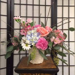 Pink and peach flowers arranged in a cream vase.