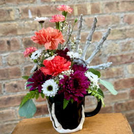 Colorful flower arrangement in a black mug with a skeletal hand decoration
