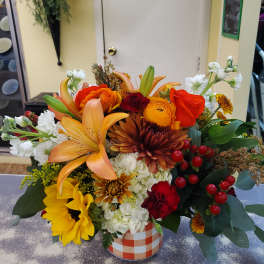 Mixed bouquet in a checkered container with lilies, roses, sunflowers, and white blooms