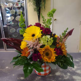 Bright mixed flower arrangement in a checkered container with sunflowers and gerberas